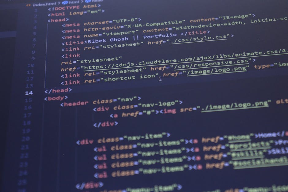 A person with short dark hair, dressed in a light blue shirt, is seated at a desk in a home or office environment, working on a laptop that displays colorful lines of code or script on the screen. The